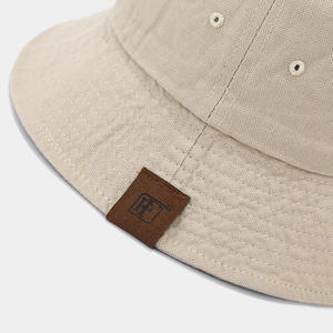 Dettaglio del cappello pescatore in tela beige con toppa logo in pelle e cuciture fini