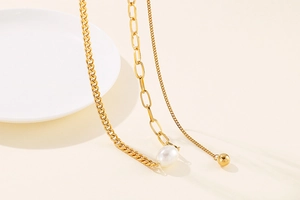 Macro shot of gold layered chain with irregular pearl and metallic ball pendant
