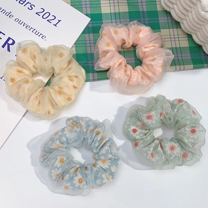 Flat lay view of sheer daisy print hair scrunchies in yellow, pink, blue and green