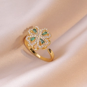 Elegant gold clover ring with green gems and white zircon on pink silk background