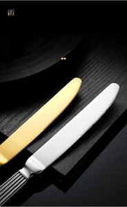 Close-up of golden and silver steak knives with sharp serrated edges on dark wood