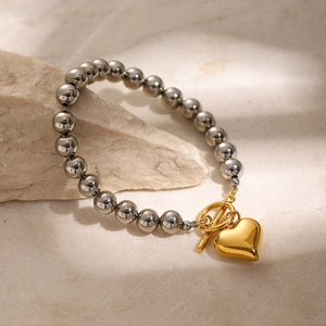 Détail de perles argentées avec pendentif cœur doré et fermoir OT sur une pierre