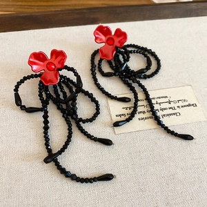 Détail de boucles d'oreilles fleur avec cristaux rouges et longs glands de perles noires