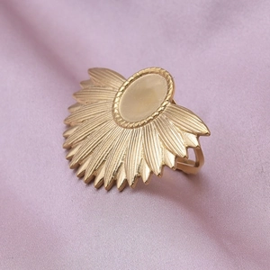 Macro shot of gold sunburst signet ring on elegant silk fabric showing textured metal rays