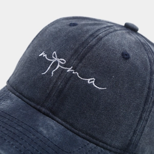 Close-up of white bow and script embroidery on a washed navy cotton baseball cap