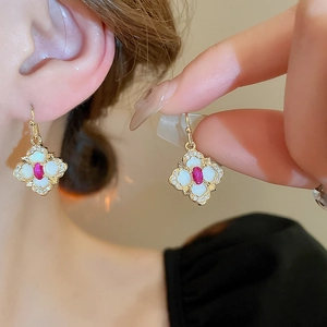 Vintage gold-plated floral earrings with red oval gemstone and white petals on a model