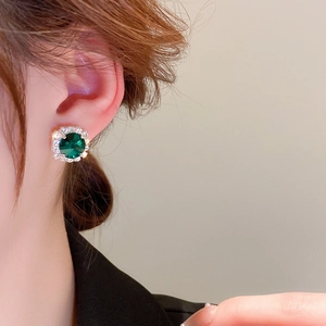 Nahaufnahme eleganter smaragdgrüner Ohrstecker mit Diamant-Halo an weiblichem Model