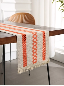 Detail of knitted table runner with orange patterns and handmade tassel fringe on wood