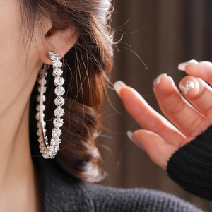 Macro shot of a model wearing large silver-colored hoop earrings set with round crystals