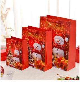 Three sizes of red Christmas gift bags with snowman and tree illustrations on a wooden table