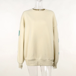 Détail du sweat-shirt crème montrant la texture du tissu et l'imprimé vert sur la manche