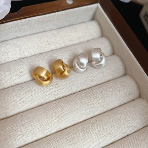 Detail view of gold and silver brushed metal knot earrings inside a beige jewelry box