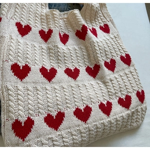 Detalle de bolso tote de punto crema con corazones rojos y textura de punto trenzado suave