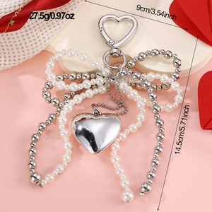 Close-up of heart charm keychain with white pearl bow and size specs on pink background