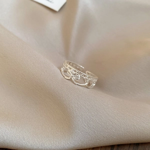 Macro shot of silver bow ring with lace hollow design on champagne silk fabric