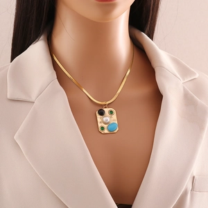 Close-up of a gold turquoise and pearl pendant necklace worn on a beige blazer