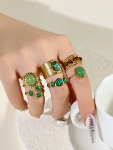 Close-up of vintage gold rings set featuring oval green and brown gemstones on hand