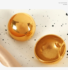 Detail view of large gold metallic ball earrings with luxury smooth texture on silk