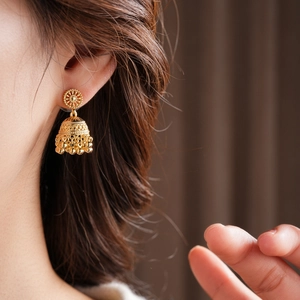 Close-up of gold Jhumka earrings with hollow bell shape and dangling beads on a model