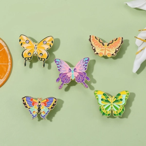 Set of five colorful enamel butterfly pins in various shades on a fresh floral background