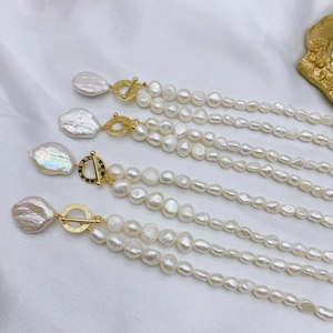Detailed view of baroque pearl necklace with golden T-bar clasp on white silk fabric