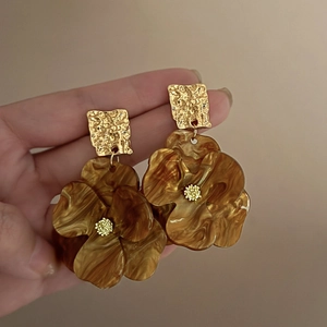 Detailed close-up of amber resin flower earrings with textured golden metal studs