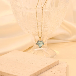 Gros plan d'une chaîne dorée avec pendentif feuille d'érable bleu clair sur cristal