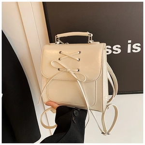 Detail of a mini cream backpack featuring a decorative bow and metallic top handle
