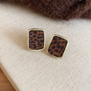 Détail de boucles d'oreilles carrées motif léopard et cadre doré sur fond de lin