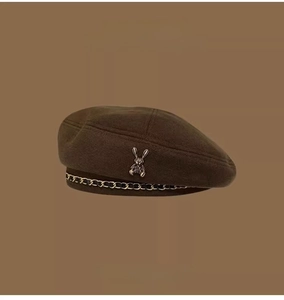 Detail of brown wool beret featuring a metallic rabbit badge and black gold chain trim