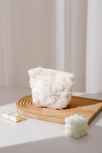 Close-up of white plush cosmetic bag with floral texture and logo on wooden tray