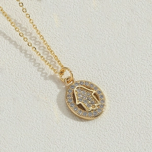 Detail of gold Hamsa pendant necklace with sparkling cubic zirconia on white background