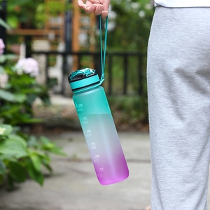Gradient sports water bottle with time markers and handle held in a natural outdoor setting