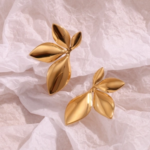 Detailed macro view of gold leaf stud earrings on textured white paper background