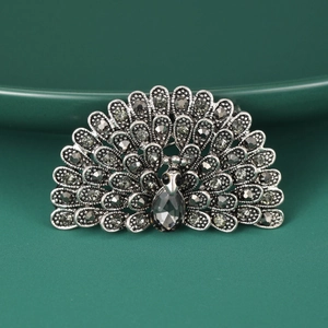 Detail of vintage peacock brooch with grey rhinestones on dark green background