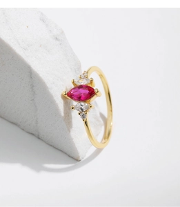 Macro shot of gold ring with marquise-cut red gemstone on white marble block
