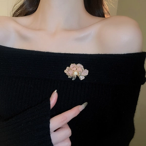 Detailed shot of pink flower brooch with gold edges and pearl on black knit garment