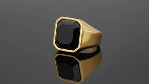 Detail view of men's gold ring with octagonal black gemstone on dark mirror