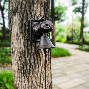 Vintage owl cast iron wall bell with antique bronze finish mounted on a garden tree