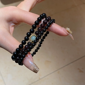 Detail of triple-layer obsidian bead bracelet with green jade and gold accents on wrist