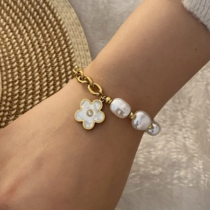 Detailed shot of gold chain bracelet with baroque pearls and white enamel flower pendant