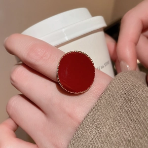 Gros plan d'une bague ronde rouge avec bordure dorée à pois sur un doigt