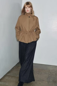 Detail of camel stand-collar jacket with waist drawstring and black button accents