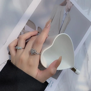 Detail of heart-shaped ring and sparkling row band worn while holding a white cup