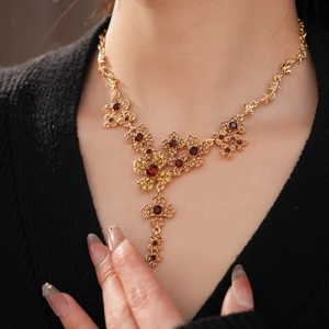 Close-up of a vintage golden floral necklace with amber and deep red gemstones on a model