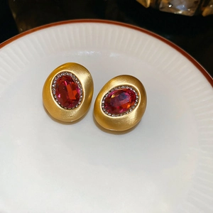 Dettaglio di orecchini ovali placcati oro 18 carati con pietre rosse su piatto ceramico
