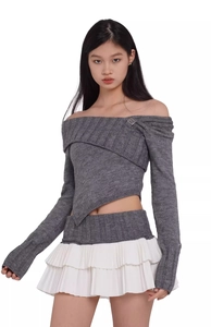 Detail of off-shoulder grey knit top with metal buckle and pleated white mini skirt