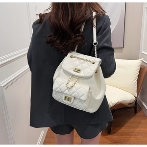 Detailed view of white quilted faux leather backpack with gold clasp and chain on model