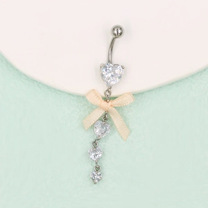 Détail d'un piercing de nombril cœur en zircon argenté avec un nœud abricot doux