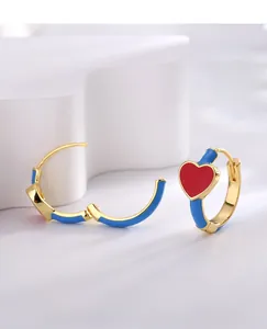 Detail of gold earrings with blue enamel hoop and a vibrant red heart charm